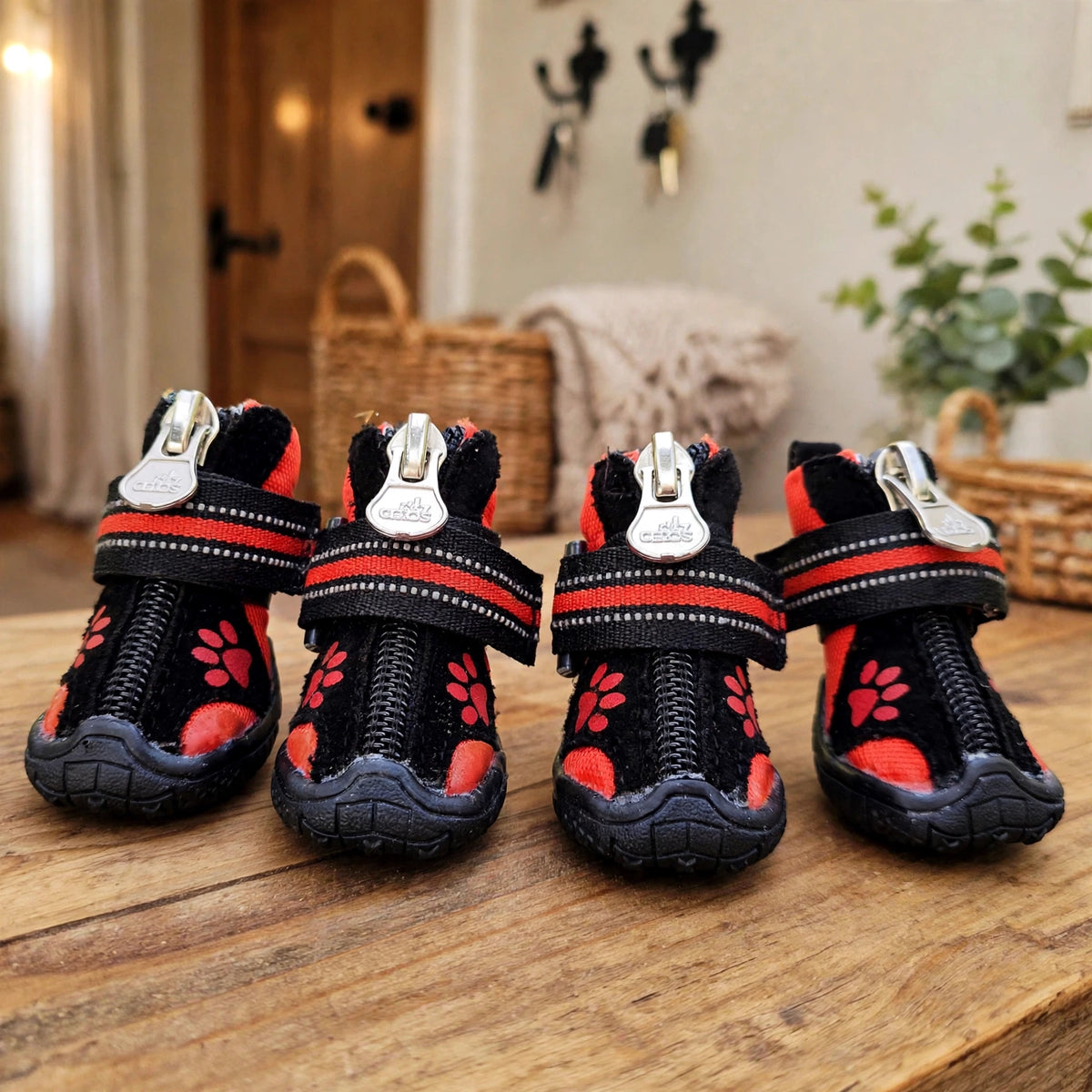 Bottes pour chien noires et rouges à motifs de pattes, avec sangle réfléchissante, posées sur une table en bois