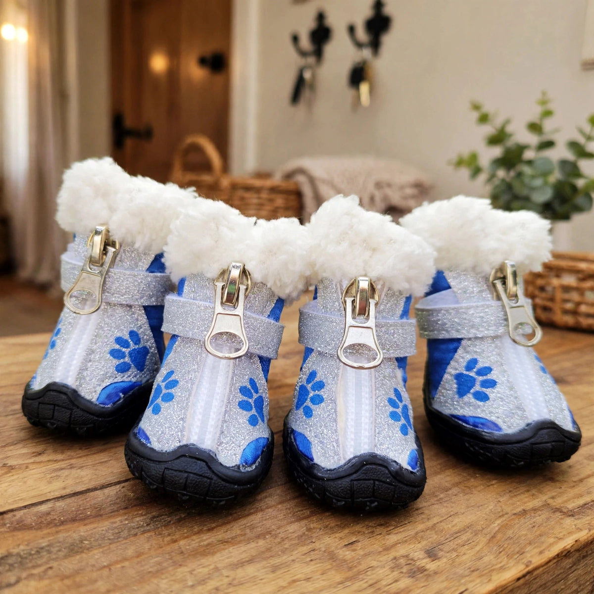 Bottes pour chien blanches et bleues à motifs de pattes et bordure en fausse fourrure, posées sur une table d'entrée en bois